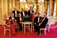 Die Mitglieder des Salonorchesters stehen mit ihren Instrumenten um einen Tisch
