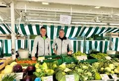 Zwei Verkäufer stehen hinter Kisten voller Gemüse