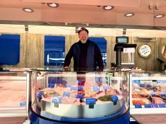 Ein verkäufer steht in seinem Verkaufswagen. Davor ist die Auslagefläche voll mit unterschiedlichen Fischsorten