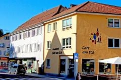 Rechts ist das orangefarbene Haus mit dem Café am Eck zu sehen, links daneben ein gauens dreistöckiges Haus mit Schaufenstern